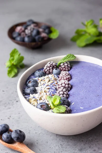 Violet magic smoothie bowl topped with blueberries, blackberries, coconut flakes and seeds. Healthy breakfast berry smoothie bowl.