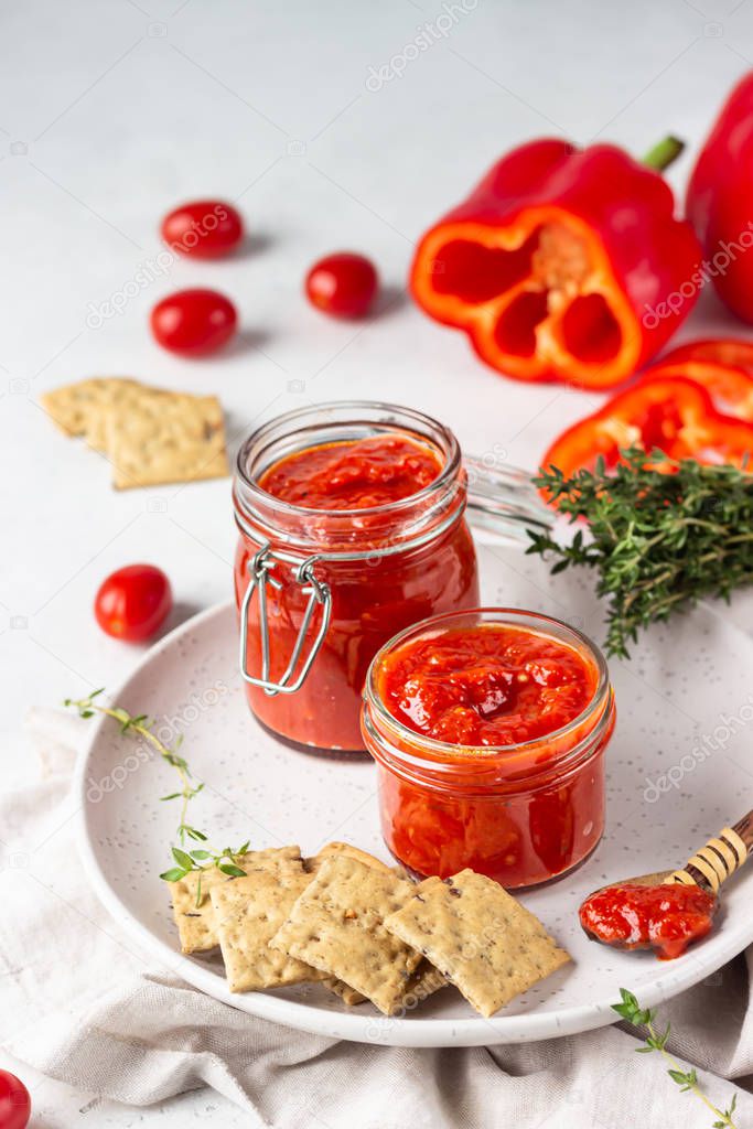 Ajvar (pepper mousse) or pindjur red vegetable spread made from paprika and tomatoes in glass jar on light stone table. Serbian native food.