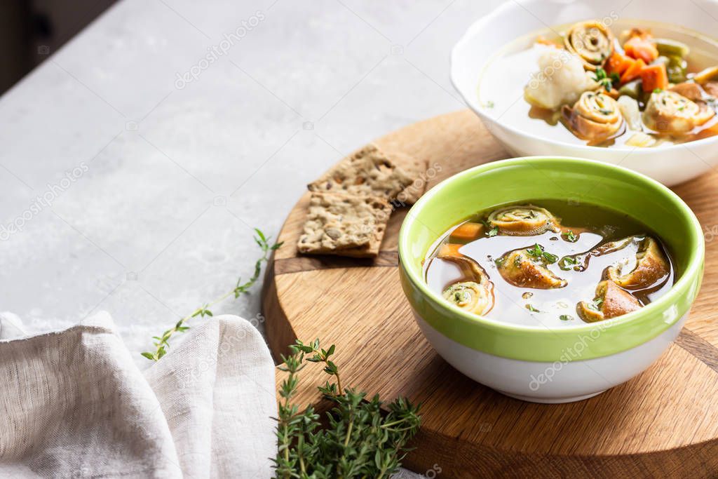 Vegetable soup with egg pancakes on light grey background. Traditional German Flaedlesuppe and Austrian Frittatensuppe. 
