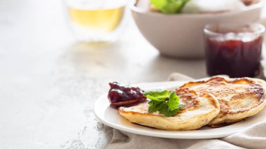 Kırmızı böğürtlen reçelli krep ve nane, bitki çayı. Amerikan mutfağı. Kahvaltı için mükemmel bir fikir. Açık gri taş arkaplan.