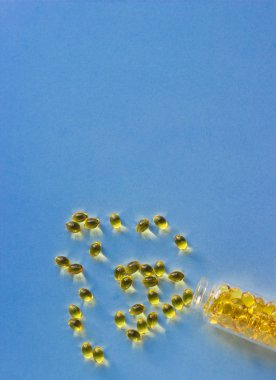 Cam bir şişede balık yağı kapsülleri (D vitamini) ve mavi kağıt arka planda. Sağlıklı ve tıbbi konsept.