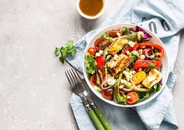 Sebze salatası kiraz domatesleri, fırında biber, salata karışımı ve ızgara haloumi (halloumi) peynirli soğan. Keto diyeti, sağlıklı yiyecekler. Açık gri taş arkaplan.