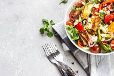 Sebze salatası kiraz domatesleri, fırında biber, salata karışımı ve ızgara haloumi (halloumi) peynirli soğan. Keto diyeti, sağlıklı yiyecekler. Açık gri taş arkaplan.