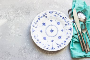 Seramik tabağın ve gümüş takımların üst görünümü, açık gri taş arkaplan.