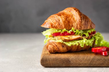 Taze kruvasan sandviçi ızgara tavuk veya hindi, dolmalık biber, sos ve salata yaprakları ahşap kesim tahtasında. Kahvaltı..