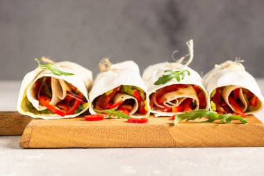 Taze vejetaryen tortilla dolmaları dolma biber, domates ve ahşap kesme tahtasında salatalık ve limon ve kırmızı biberle birlikte. Açık gri taş arkaplan. 