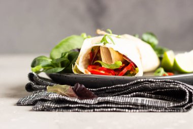 Vejetaryen tortilla sandviç paketler, sebze salatalı sandviç sarar yeşil salata karışımı, limon ve kırmızı biber ile servis edilir siyah seramik tabakta.
