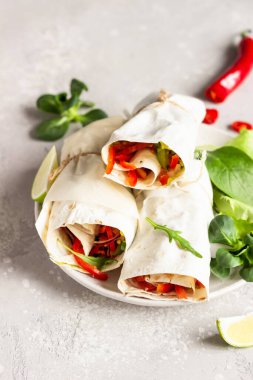 Üç taze vejetaryen tortilla sandviç sarar, sebze salatalı sandviç sarar yeşil salata karışımı, limon ve acı biber seramik tabakta servis edilir..