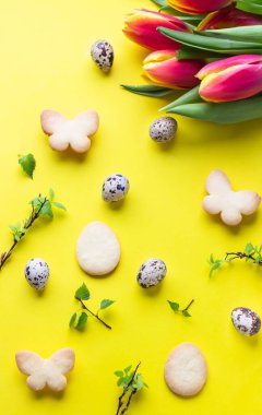 Paskalya kurabiyeleri, kırmızı ve sarı laleler, sarı kağıtta bıldırcın yumurtaları. Paskalya sembolleri ve gelenekler. Tereyağlı ve şekerli kurabiye.