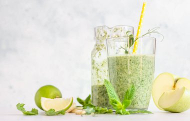 Bardaktaki malzemelerle karıştırılmış yeşil smoothie ve açık gri masada sürahi. Detoks, diyet, sağlıklı, vejetaryen gıda konsepti.