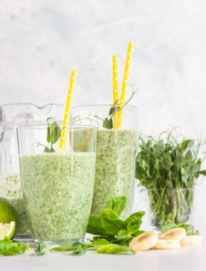 Ispanak, muz, kireç, nane ve taze filizli yeşil smoothie açık gri taşlı arka planda.