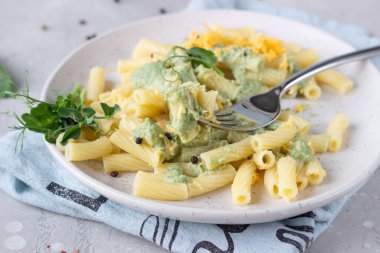 Yeşil krem soslu makarna, seramik tabakta peynir ve mikro yeşiller, açık gri taş zemin. İtalyan yemeği.. 