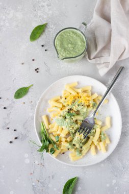 Yeşil krem soslu makarna, seramik tabakta peynir ve mikro yeşiller, açık gri taş zemin. İtalyan yemeği. Üst görünüm. 