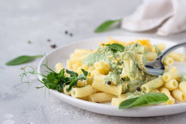 Yeşil krem soslu makarna, seramik tabakta peynir ve mikro yeşiller, açık gri taş zemin. İtalyan yemeği.. 