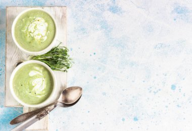 Yeşil sebzelerden arınma kremi çorbası (brokoli, yeşil bezelye, ıspanak) krema, limon aroması ve gri beton arka planda mikro yeşilliklerle servis edilir. Temiz yemek, sağlıklı yemek konsepti. Üst görünüm. 