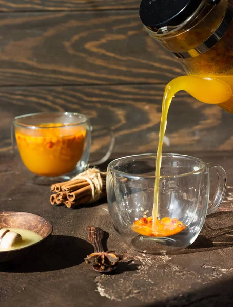 Process brewing tea, hot colorful sea buckthorn tea is poured into a glass cup.