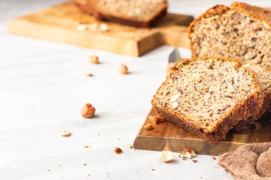 Ev yapımı muz ekmeği ya da tahta kesme tahtasının üzerinde fındıklı kek, hafif taş arka plan. Modaya uygun yumuşak gölgeler, atmosferik aydınlatma, seçici odaklanma. Düz konum.