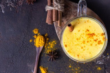 Baharatlı zerdeçal (curcuma) tozlu altın süt veya latte, koyu kahverengi beton arka plan. Moda detoks, bağışıklık güçlendirici, iltihap önleyici sağlıklı içecekler.. 