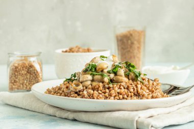 Mantarlı karabuğday lapası ve açık gri beton arka planda seramik tabakta otlar. Vejetaryen ve vejetaryen yemeği. Sağlıklı içerik. Tonu ayarlanmış resim. 