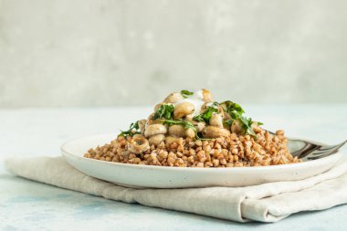 Mantarlı karabuğday lapası ve açık gri beton arka planda seramik tabakta otlar. Vejetaryen ve vejetaryen yemeği. Sağlıklı içerik. Tonu ayarlanmış resim. 