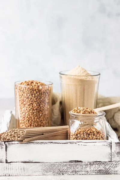 Uncooked organic buckwheat grains, buckwheat flour and buckwheat soba noodles in a wooden tray, light grey concrete background. Healthy concept.