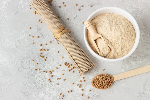 Buckwheat flour in bowl, small wooden scoop with flour and dried soba noodles. Healthy diet, gluten free products.