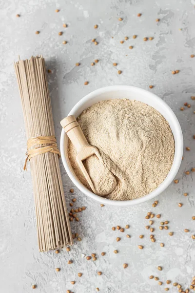 Buckwheat flour in bowl, small wooden scoop with flour and dried soba noodles. Healthy diet, gluten free products. Top view.