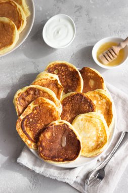 Ballı ve ekşi kremalı ev yapımı krepler, güneşli gölgeli masa yüzeyi. Açık gri beton arka plan. Doğal ışık ve gölgeler yiyecek fotoğrafçılığı konsepti. Kahvaltıda. Üst görünüm. 