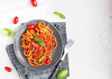 Makarna, domates soslu spagetti, taze domates ve siyah seramik tabakta fesleğen. Gri taş arka plan. Üst görünüm. 