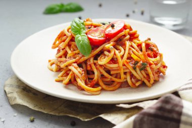 Domates soslu, fesleğenli ve seramik tabakta taze vişneli domatesli vejetaryen iştah açıcı makarna. Açık gri beton arkaplan. 