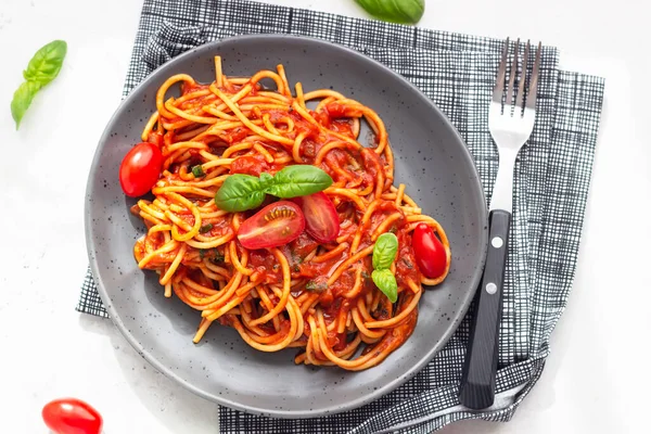 Pasta, spaghetti with tomato sauce, fresh tomatoes and basil in black ceramic plate. Grey stone background. Top view.