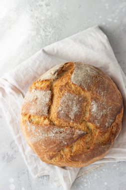 Keten peçeteye konmuş buğday ve çavdar unundan yapılmış tam bir rustik ekmek, açık gri taş zemin. Seçici odaklanma. Üst görünüm.