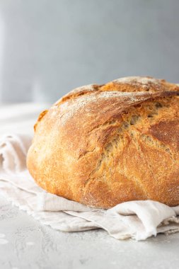 Keten peçeteye konmuş buğday ve çavdar unundan yapılmış tam bir rustik ekmek, açık gri taş zemin. Seçici odak. 