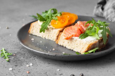 Buğday, çavdar ekmeği, domates, füme somon ve roka ile açık sandviç, gri beton arka plan. Seçici odak. 