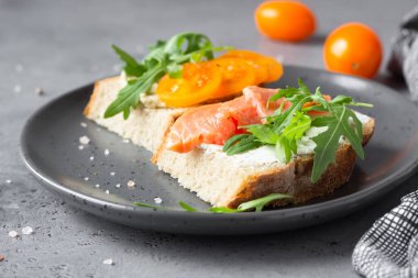 Buğday, çavdar ekmeği, domates, füme somon ve roka ile açık sandviç, gri beton arka plan. Seçici odak. 