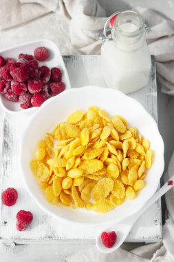 Mısır gevreğiyle sağlıklı bir kahvaltı ve ahududulu bir kasede süt, açık gri arka plan. Seçici odak. 