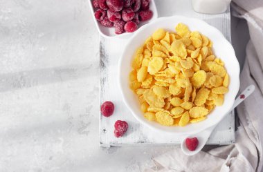 Mısır gevreğiyle sağlıklı bir kahvaltı ve ahududulu bir kasede süt, açık gri arka plan. Seçici odaklanma. Üst görünüm.