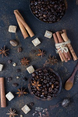 Aromatik kahve çekirdekleri, anason yıldızları, tarçın çubukları, esmer şeker küpleri ve koyu kahverengi beton arka planda hindistan cevizi. Noel pastası ve içecekleri için baharatlar..