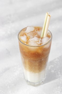 Sütlü ve buzlu soğuk kahve uzun bir bardakta bambu kamışı, açık gri arka plan. Seçici odak. 
