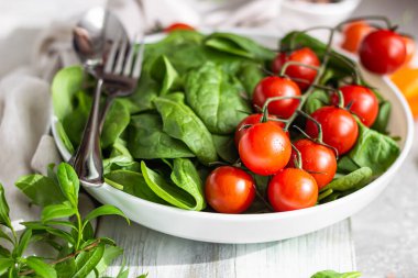 Beyaz seramik tabakta bebek ıspanak, kırmızı kiraz ve sarı domates. Taze sebzeler. Yaz hasat konsepti.