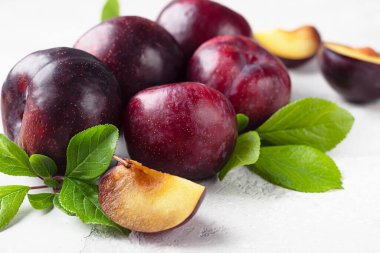 Olgun sulu mor erikler, bütün ve yapraklı dilimler. Açık gri taş arka plan. Sağlıklı vejetaryen yemekleri.