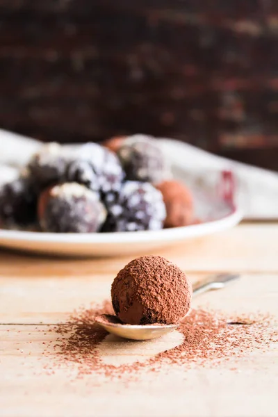 Chocolate truffles with cocoa, nuts and coconut on a dessert plate on a wooden rustic table, selective focus