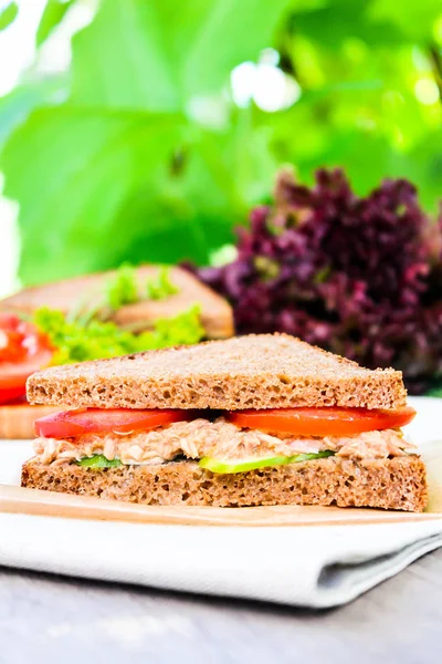 Sandwich with rye brown bread, ripe tomatoes, cucumbers and tuna fish for healthy snack on a napkin on a wooden table, selective focus