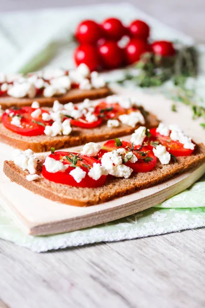 Homemade traditional italian snack Bruschetta with cherry tomatoes, salted feta cheese and thyme on a wooden cutting board, selective focus