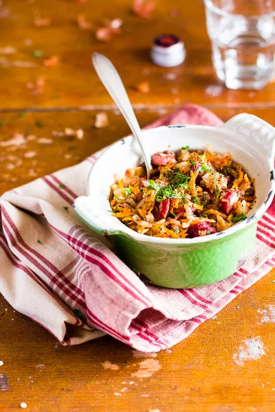 Traditional polish food. Bigos, stewed cabbage with carrot, onion, green lentil and pork meat sausages in a pot on a wooden table, selective focus. German cuisine. Comfort food.