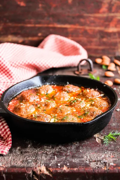 Cooking pan with meatballs in tomato sauce with spices and almond nuts on a wooden table, selective focus. Image with copy space. Meatballs are made of minced pork and beef meat. American food.