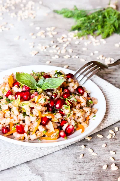 Plate of pearl barley warm salad with carrot, dill and pomegranate seeds in a plate on a wooden table, selective focus. Healthy and organic food concept. Fasting food. Vegetarian food.