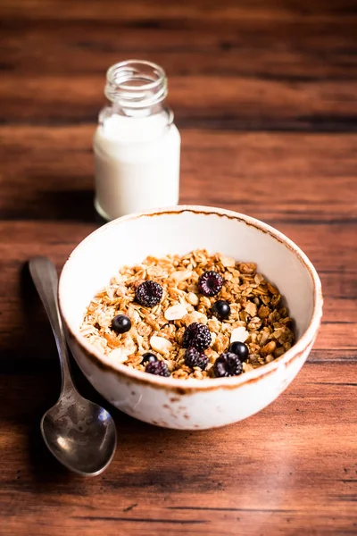 Breakfast super bowl of homemade granola or muesli with oat flakes, black currant, black raspberry and peanuts on a wooden table, selective focus. Served with a bottle of fresh milk. Organic food.