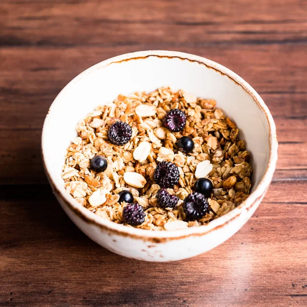 Breakfast super bowl of homemade granola or muesli with oat flakes, black currant, black raspberry and peanuts on a wooden table, selective focus. Served with a bottle of fresh milk. Organic food.