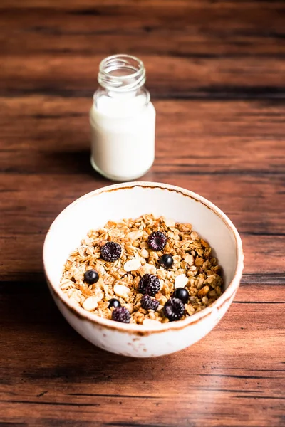 Breakfast super bowl of homemade granola or muesli with oat flakes, black currant, black raspberry and peanuts on a wooden table, selective focus. Served with a bottle of fresh milk. Organic food.
